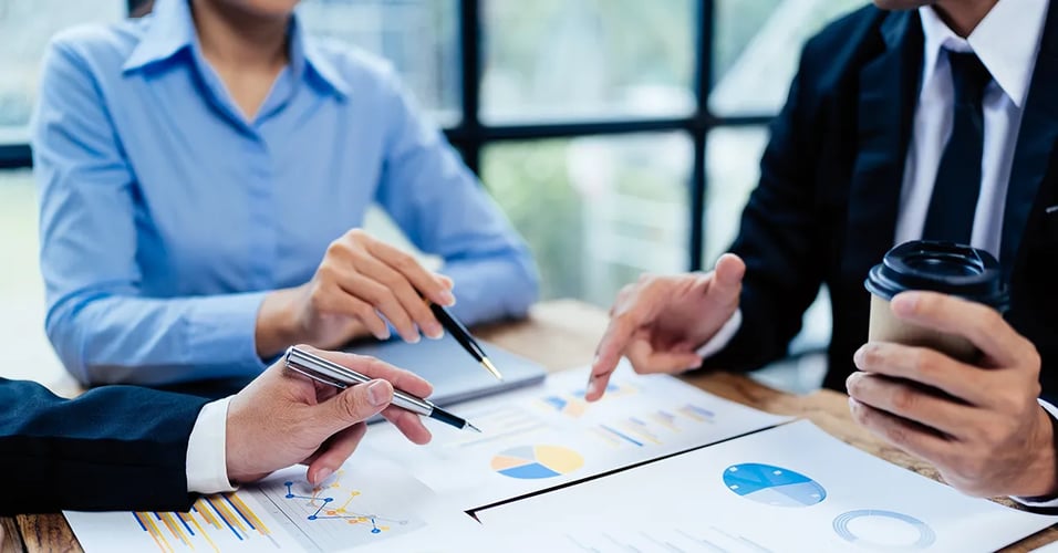 People using pens to point at graphs on table.