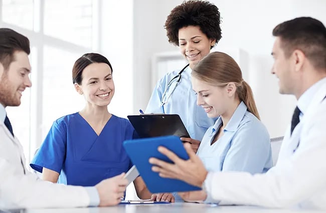 Group of healthcare workers reviewing clipboards and tablet devices together