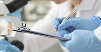 Hand wearing latex gloves writing on clipboard near medical equipment