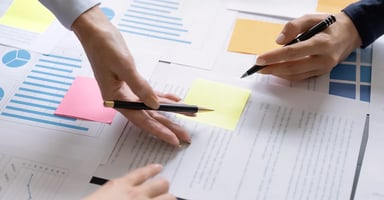 Hands and pens pointing to papers and post-it notes