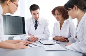 healthcare-workers-labcoats-reviewing-papers-near-computer-monitor-ss-46716574-650x425