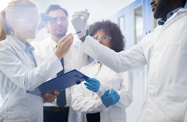 Medical professionals wearing lab coats reviewing fluid in test tube