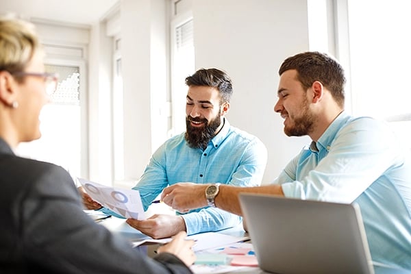 professionals-around-conference-table-smiling-pointing-at-papers-with-data-graphs