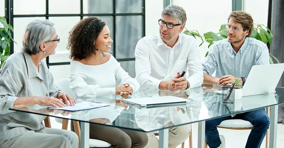 Several business professionals talking around glass conference table