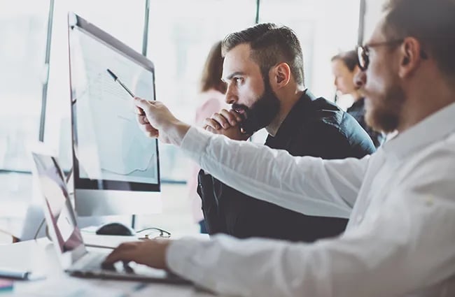 Two data professionals reviewing data on computer monitor