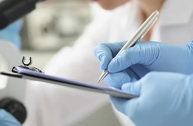 Hand wearing latex gloves writing on clipboard near medical equipment