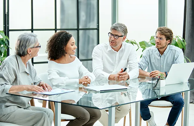 Several business professionals talking around glass conference table